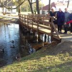 Seniorzy stoją na mostku i karmią kaczki w stawie